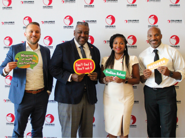 four district administrators stand in front of a step and repeat smiling while holding math signs